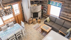 A cozy log cabin interior with a stone fireplace, a television, a dining area with a table and chairs, and a sofa. - Rukajoiku 1 by Interhome (Kuusamo)