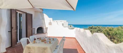 A terrace with a table set for dining, overlooking a coastal view.