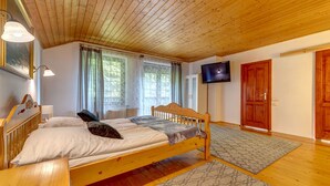 Un lit en bois avec une tête de lit, une table de chevet, un téléviseur fixé au mur et une grande fenêtre avec des rideaux.
