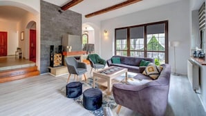 Un salon spacieux doté d’une cheminée, de poutres apparentes, d’une grande fenêtre et d’un coin salon confortable.