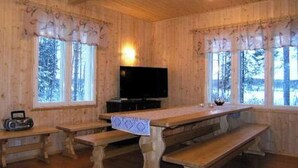 A wooden cabin with a long dining table, benches, a television, and large windows.