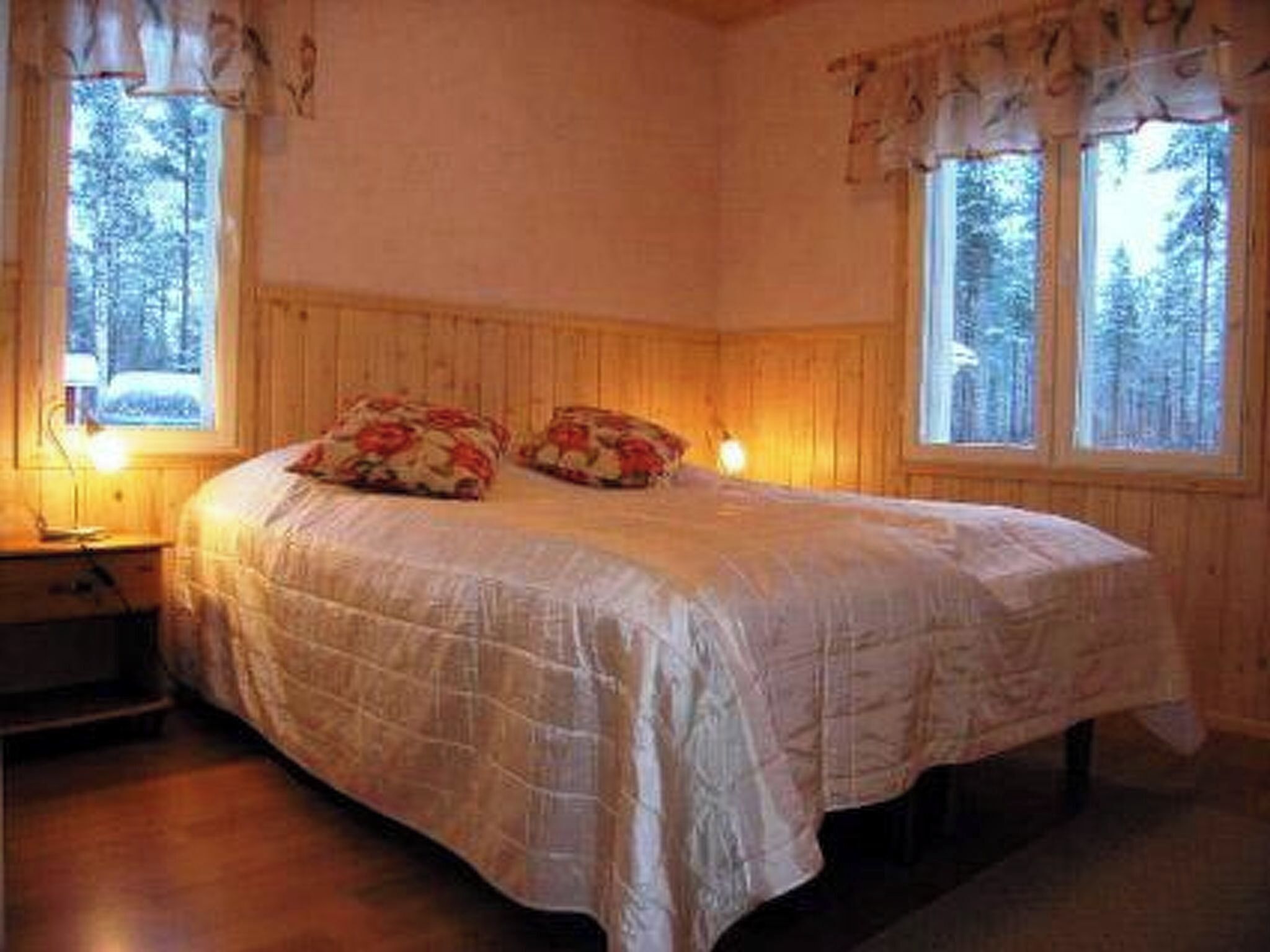 Ein Schlafzimmer mit einem Bett, zwei Nachttischen und zwei mit Vorhängen versehenen Fenstern.