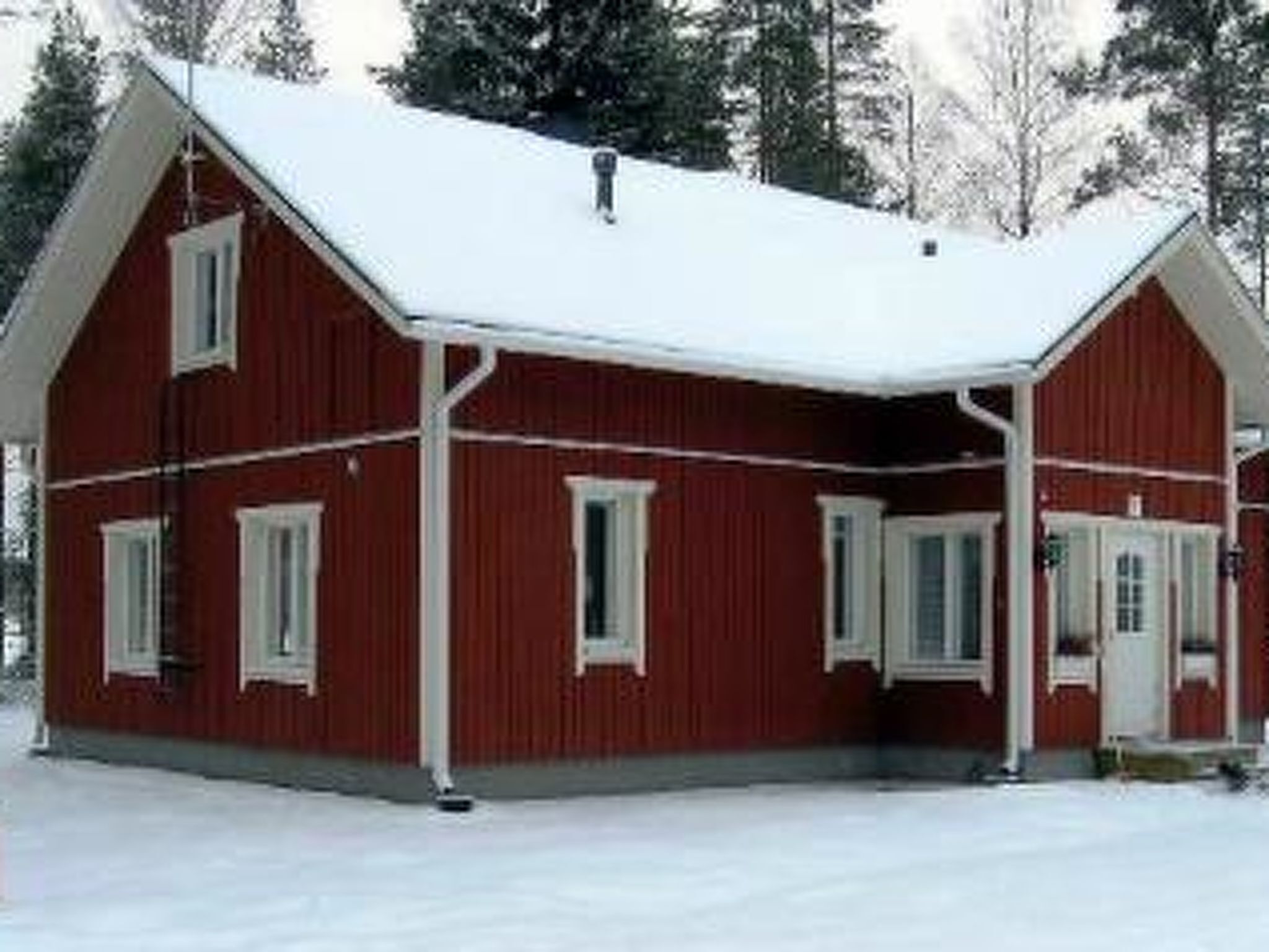 A red wooden house with a snow-covered roof and white trim.