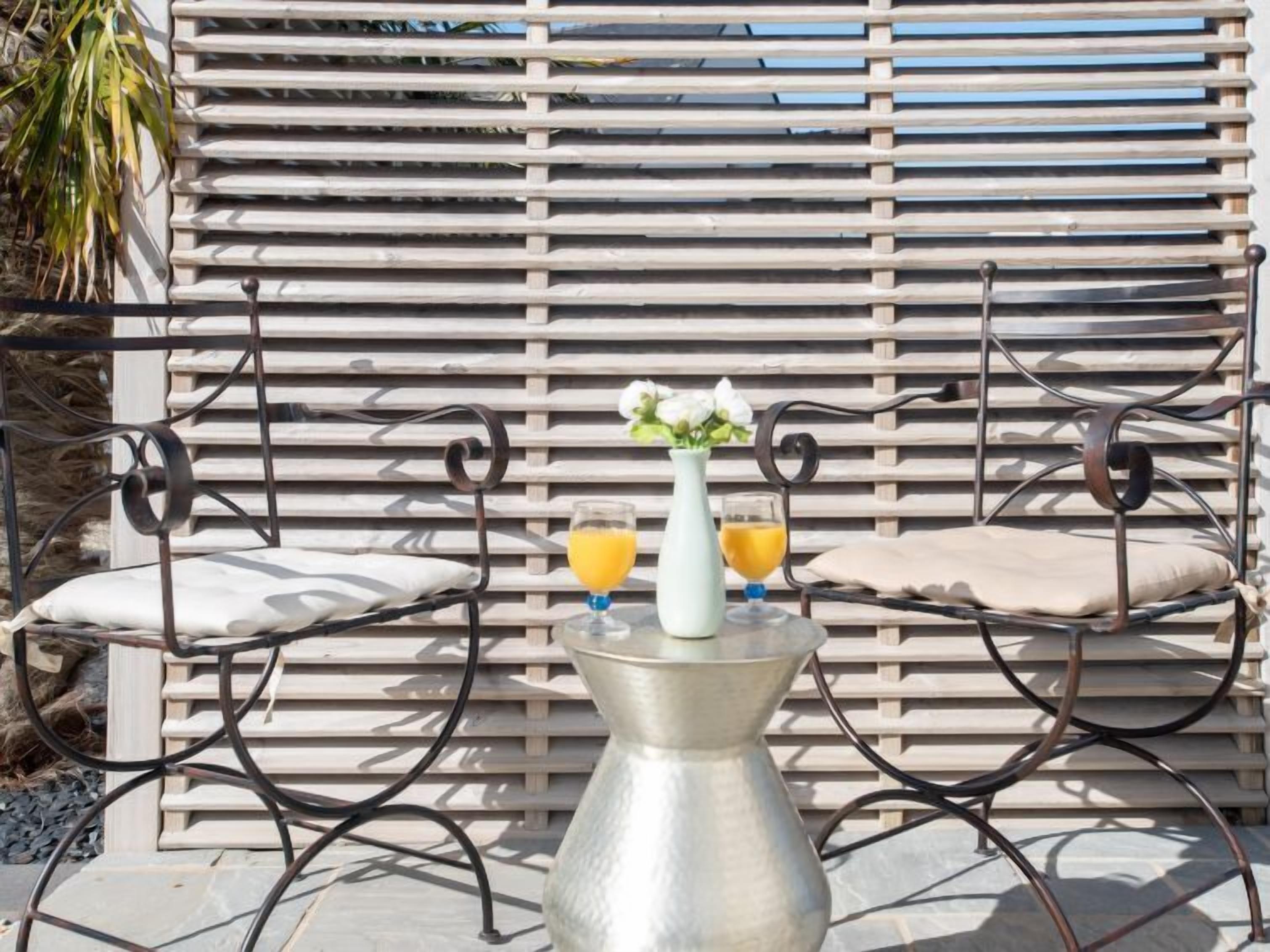 Un espace extérieur aménagé avec des sièges, doté d’une structure en métal, comprenant deux fauteuils rembourrés et une table en métal.