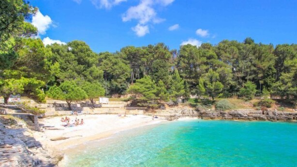 Una playa con agua turquesa cristalina, arena blanca y acantilados rocosos.