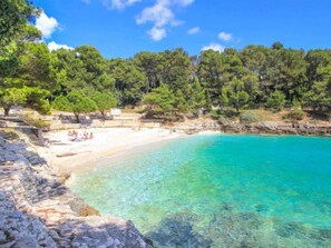 A beach with clear turquoise water, white sand, and rocky cliffs. - Iris Croatica by Interhome (Pula)