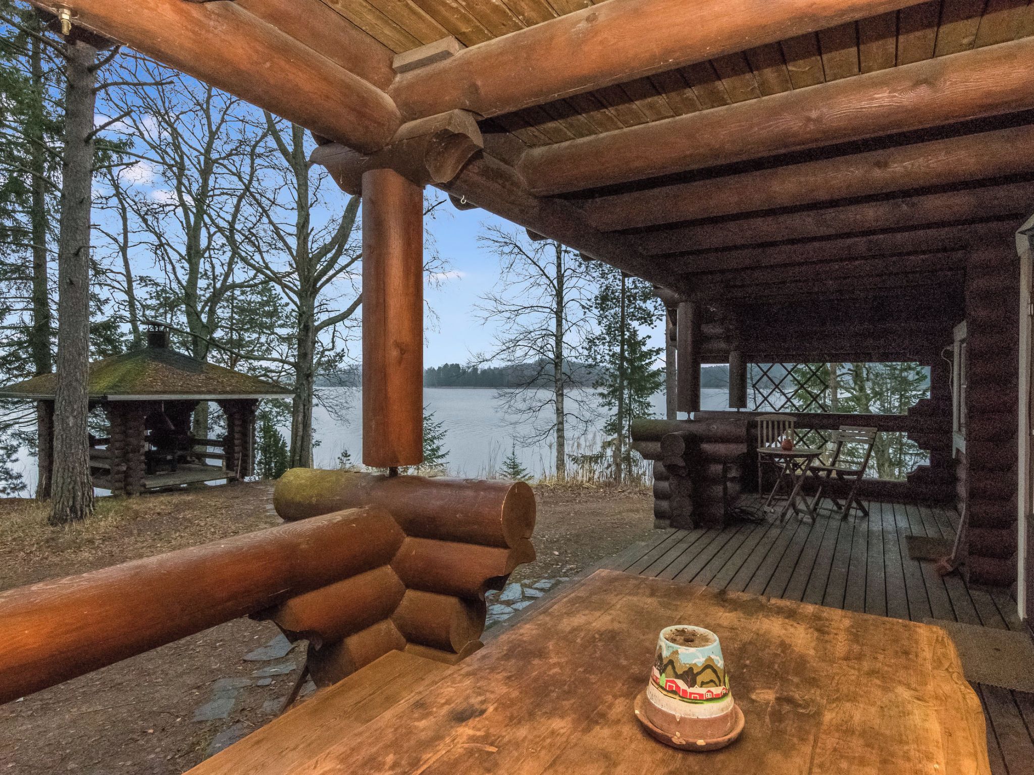 A wooden deck with a table and chairs, overlooking a lake.
