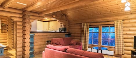 A log cabin interior with a sofa, a dining table, and a kitchen area.