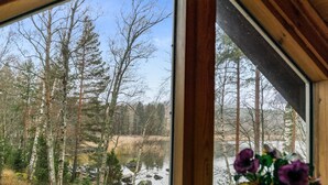 A room with a large window offering a view of a forest and a body of water.