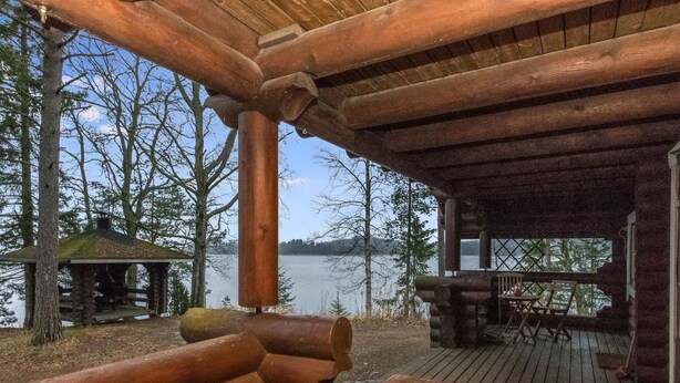 A wooden cabin with a deck overlooking a lake, featuring a table with a hat and a rustic wooden bench.
