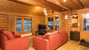 A log cabin interior with a sofa set, a television, and wooden walls.