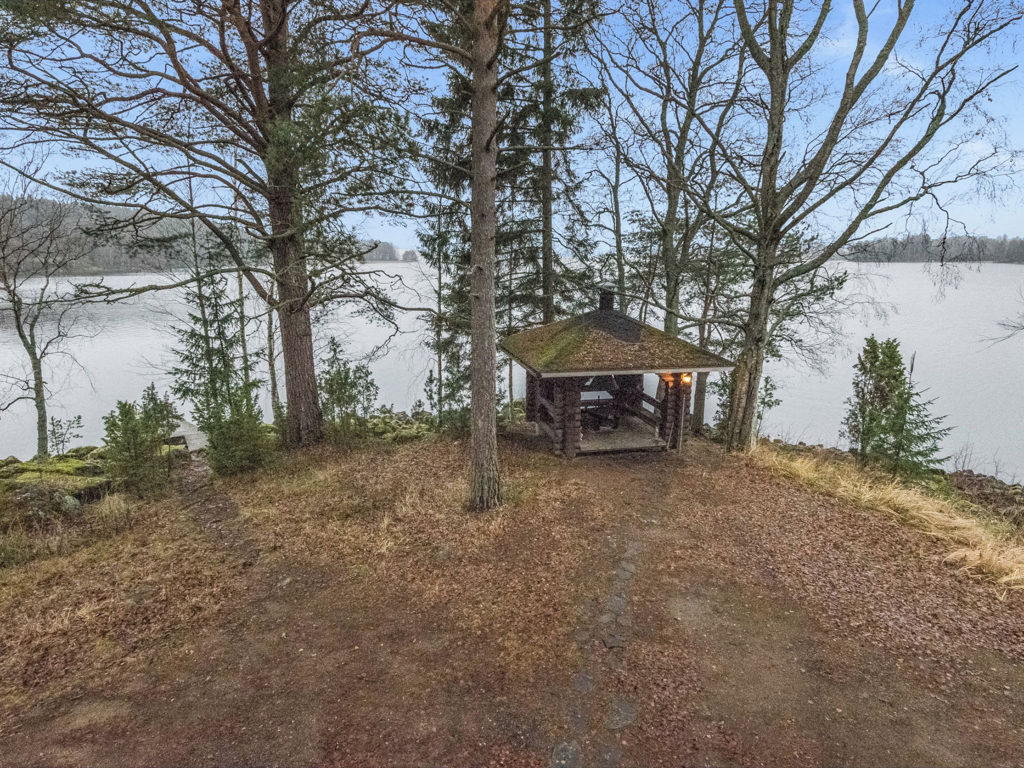 A wooden structure with a roof, surrounded by trees and a body of water.