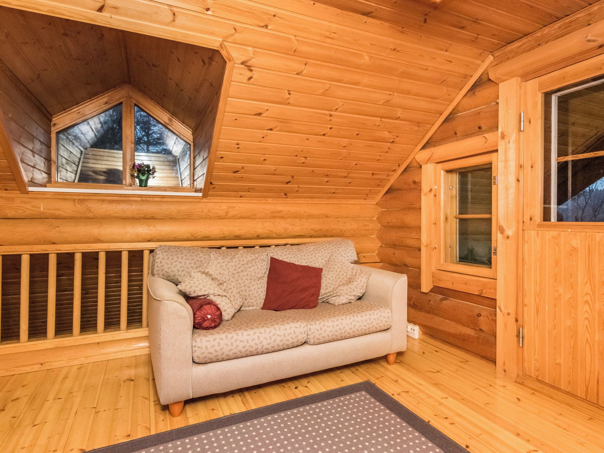 L'interno accogliente di una baita, con soffitto in legno, un divano con cuscini decorati, una finestra vista e una porta.