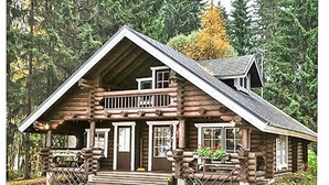 A log cabin with a front porch, a balcony, and a chimney.