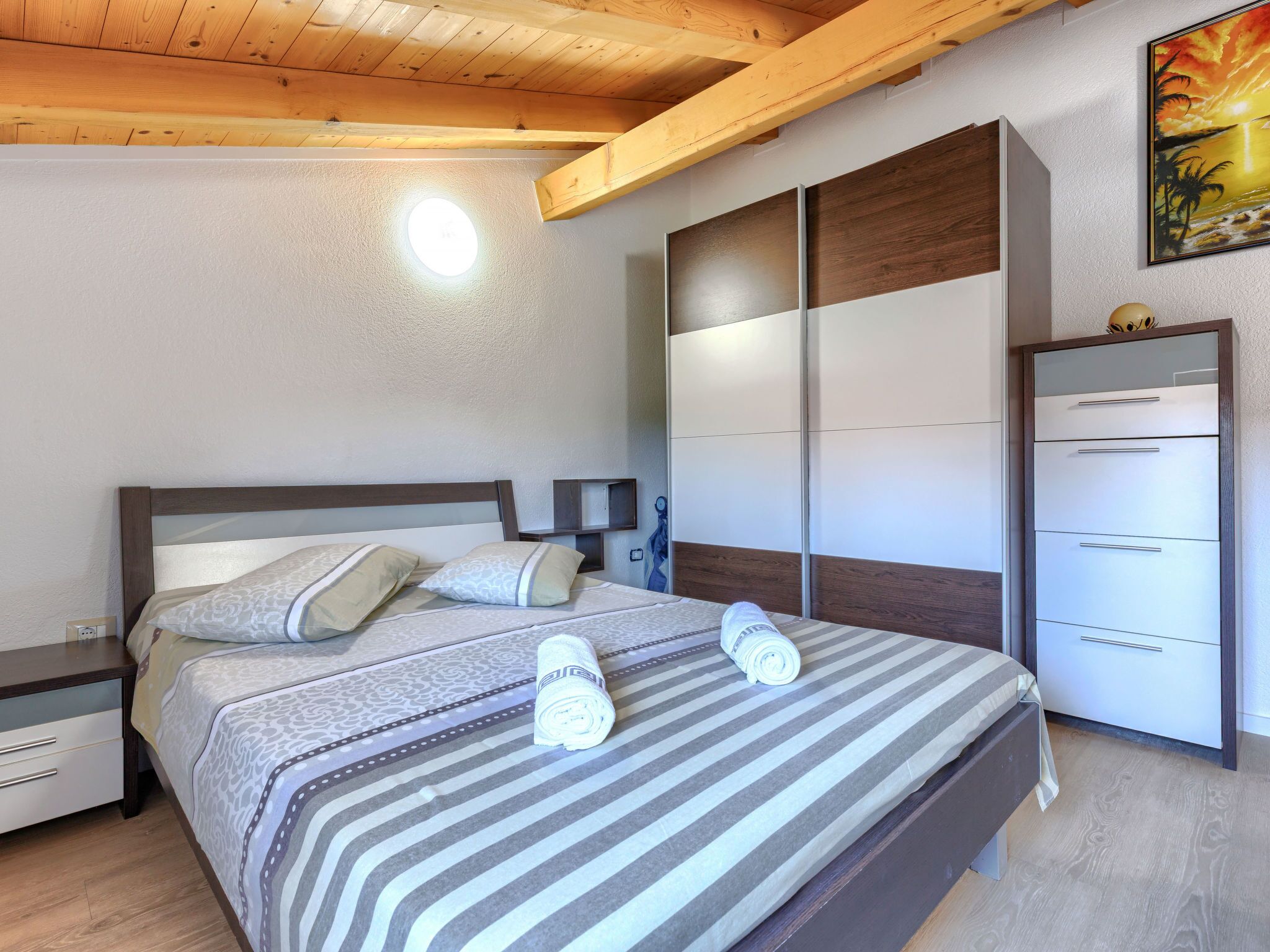 A bedroom with a bed, nightstands, a wardrobe, and a painting on the wall.