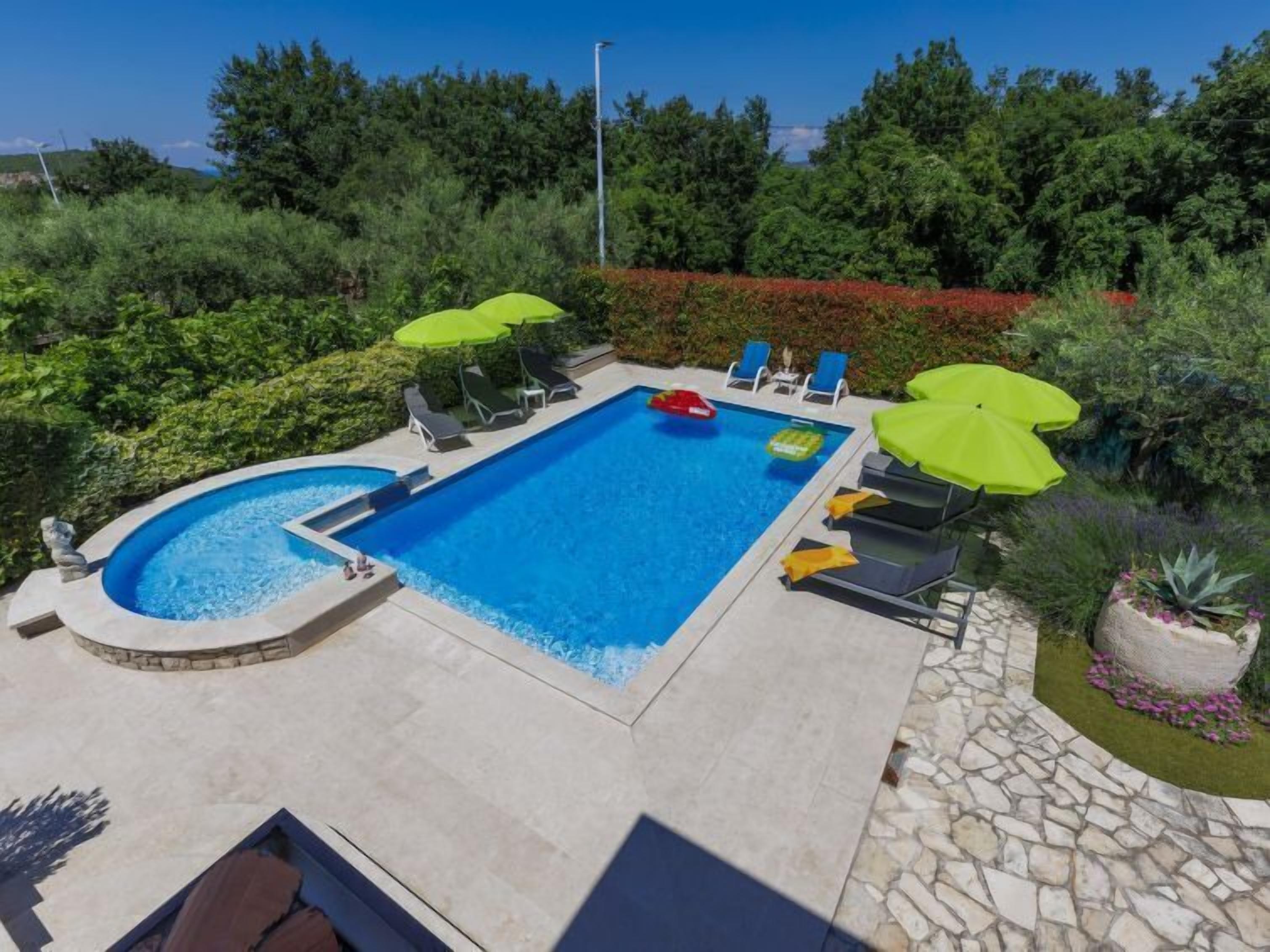 A rectangular swimming pool with a stone border, surrounded by lounge chairs and umbrellas.
