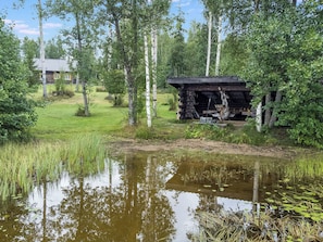 A rustic cabin surrounded by a pond with reflections, a grassy area, and birch trees. - Runopuro by Interhome (Rautalampi)