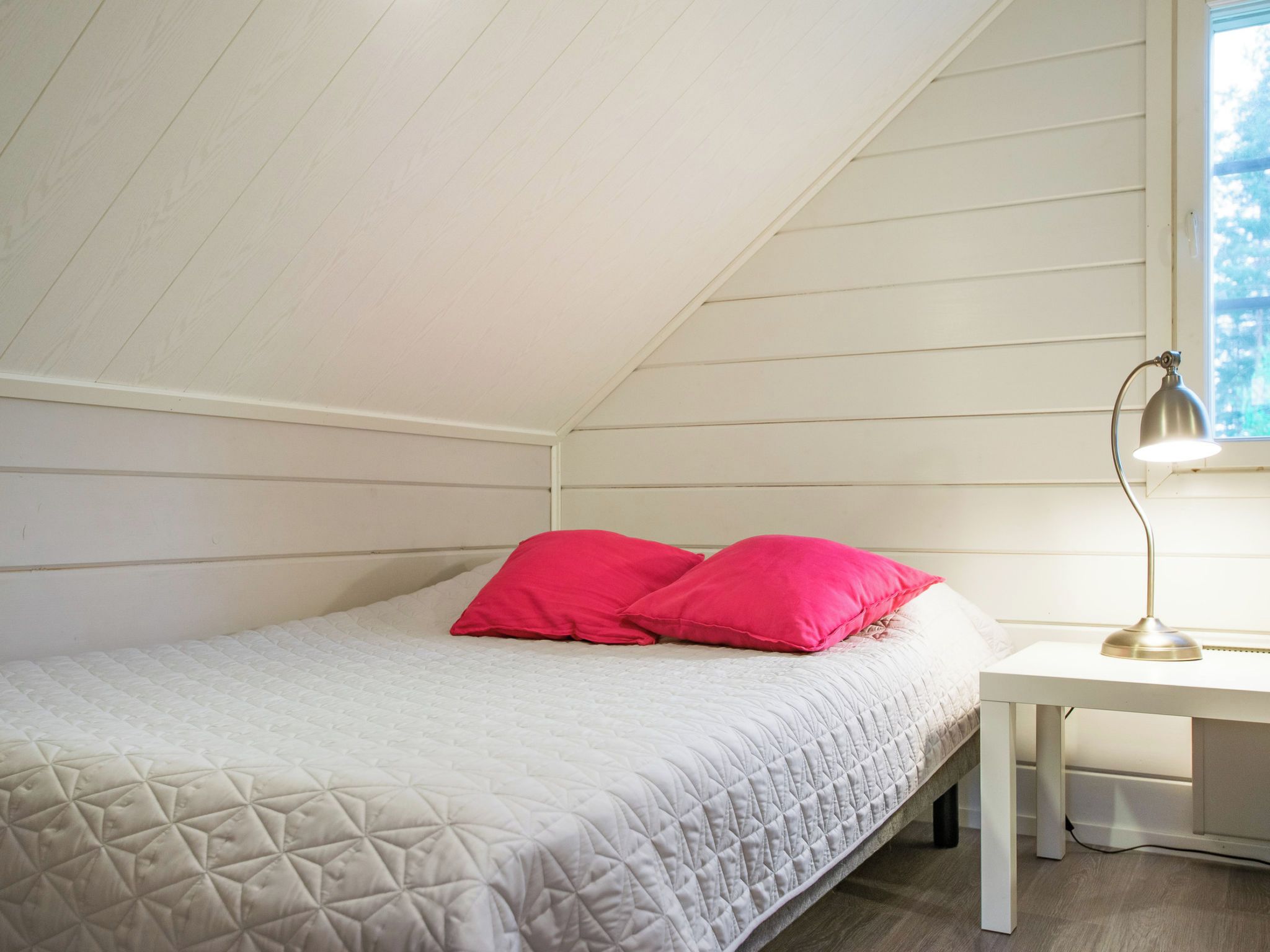A bedroom with a bed, two pillows, a bedside table, and a lamp.