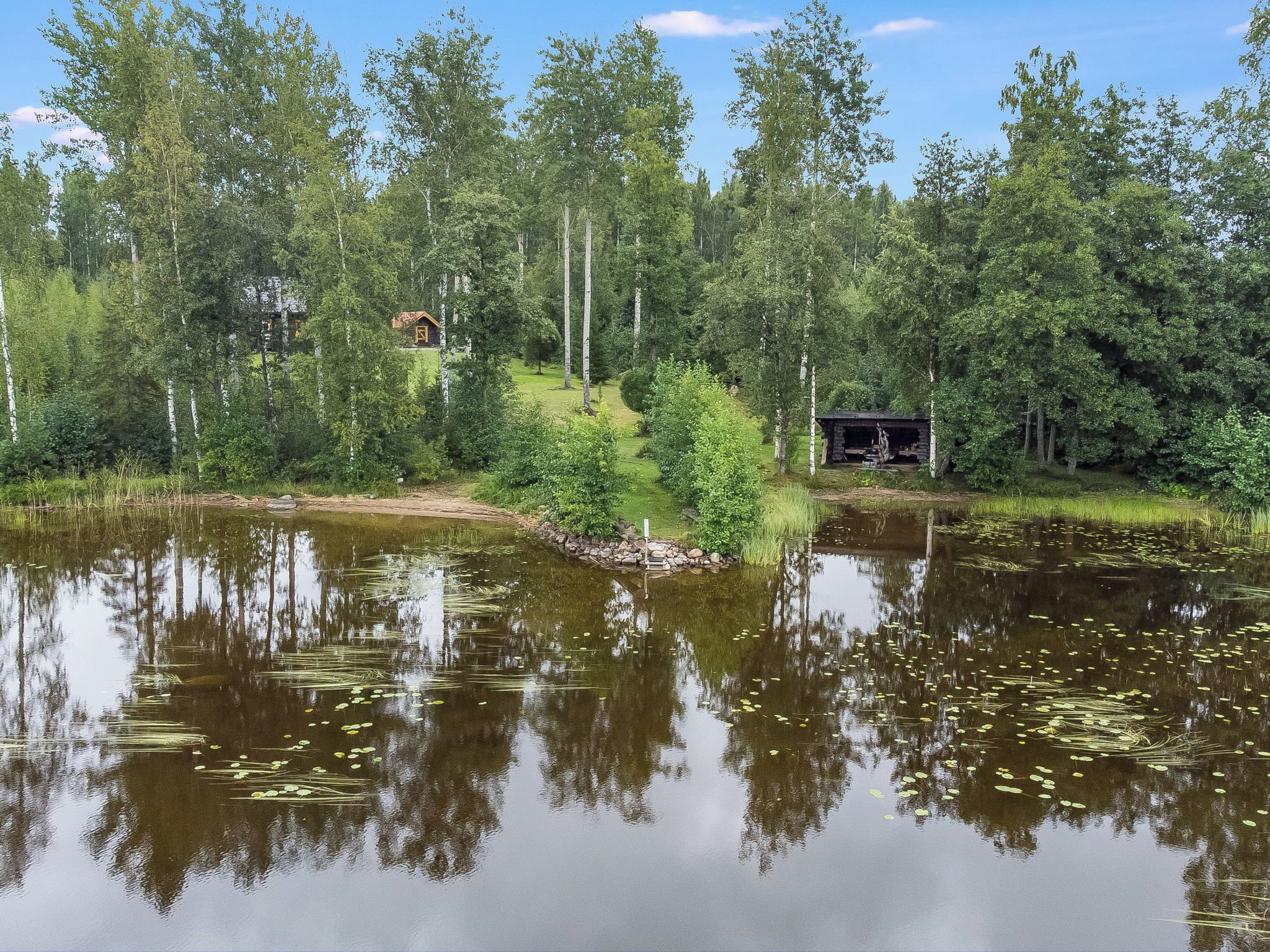 A serene lakeside setting with a cabin and a small structure surrounded by dense forest.
