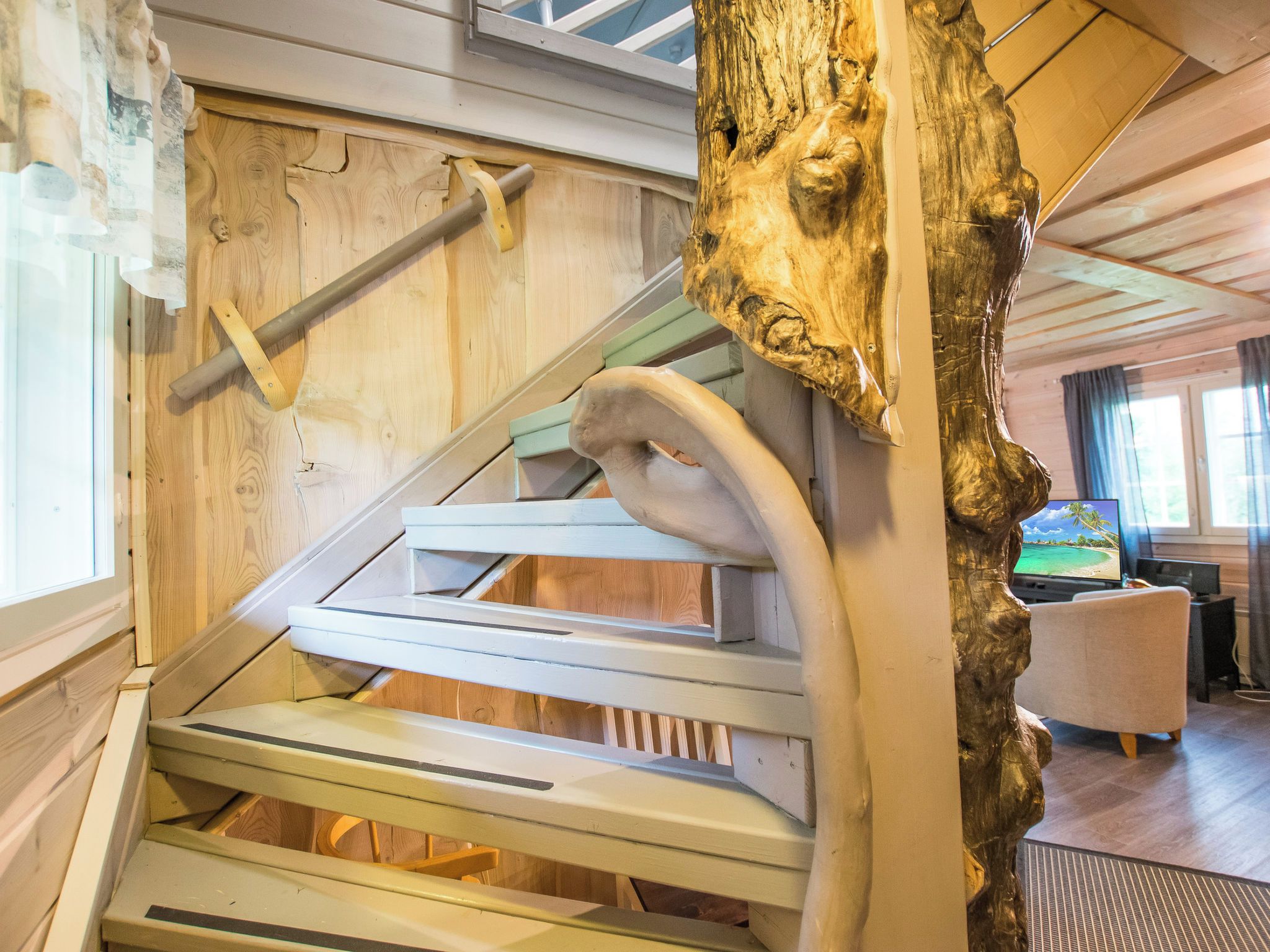 A wooden staircase with a unique design, leading to a room with a television and a chair.