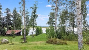 A grassy area with birch trees, a small wooden cabin, and a lake in the background. - Runopuro by Interhome (Rautalampi)