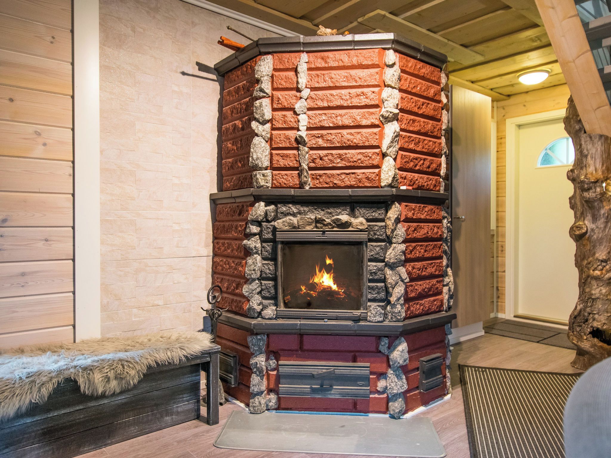A stone fireplace with a fire, surrounded by a wooden bench and a rug.