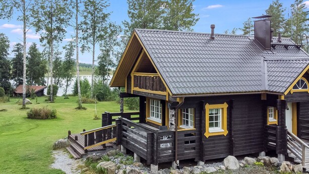 A wooden cabin with a porch, a chimney, and a view of a lake. - Runopuro by Interhome (Rautalampi)