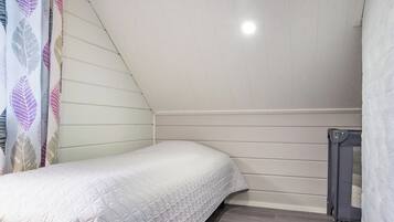 A small, single-bed room with a sloped ceiling, a radiator, and a patterned curtain.