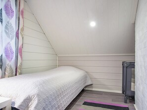 A small, single-bed room with a sloped ceiling, a radiator, and a patterned curtain. - Runopuro by Interhome (Rautalampi)