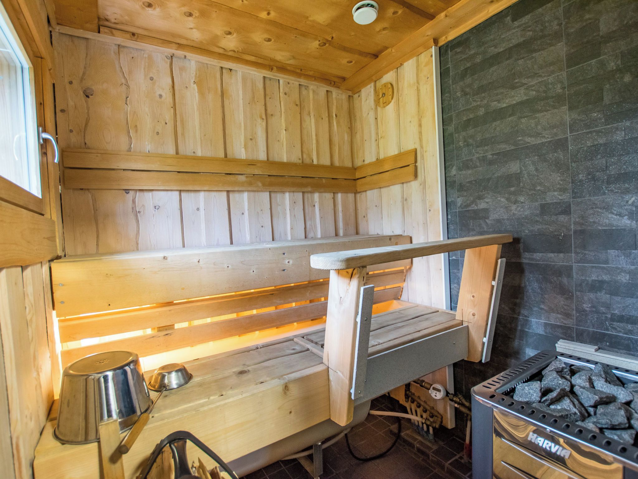 Un sauna avec des bancs en bois, un mur en pierre et un appareil de chauffage de sauna de la marque Harvia.