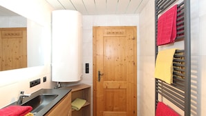 A modern bathroom with a wooden door, a sink with a mirror, and a towel rack with multiple towels. - Katharina by Interhome (Aschau im Zillertal)