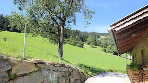 A stone wall leading to a wooden building with a covered porch, surrounded by a green landscape and trees. - Katharina by Interhome (Aschau im Zillertal)