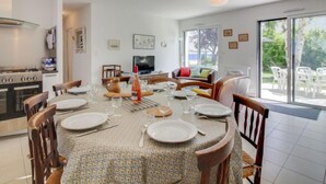 Ein Essbereich mit rundem Tisch für sechs Personen, eine Küche mit Herd und Backofen sowie ein Wohnbereich mit Fernseher und Sofa.