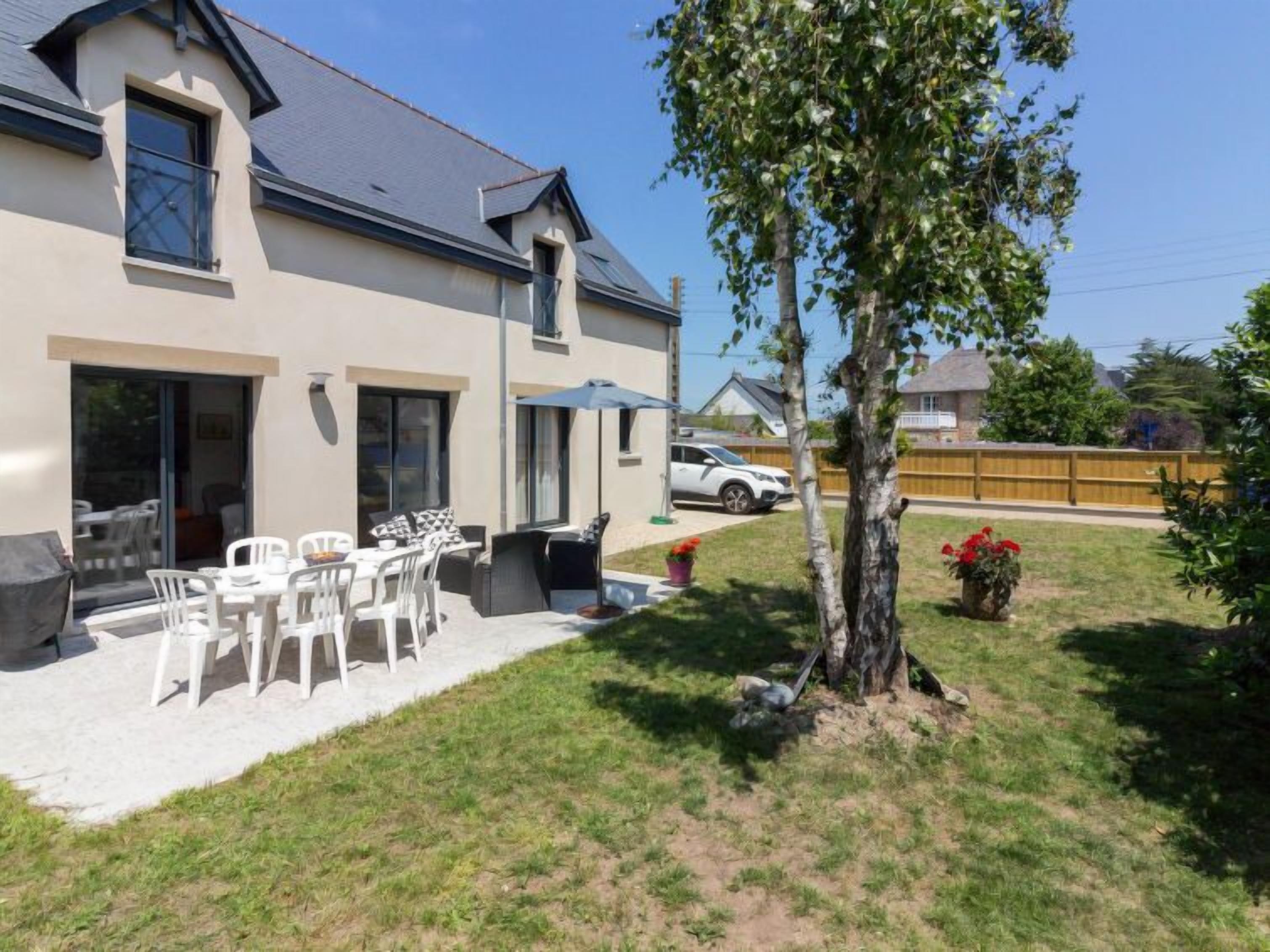 Une maison à deux étages dotée d’un patio aménagé avec du mobilier d’extérieur et un arbre.