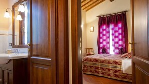 Un dormitorio con cama, mesita de noche, espejo y ventana con cortinas.