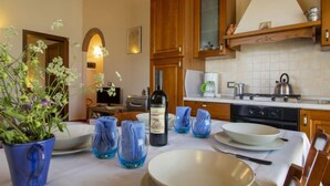 Una cocina con armarios de madera, una estufa y una mesa de comedor dispuesta con platos, tazones y una botella de vino.