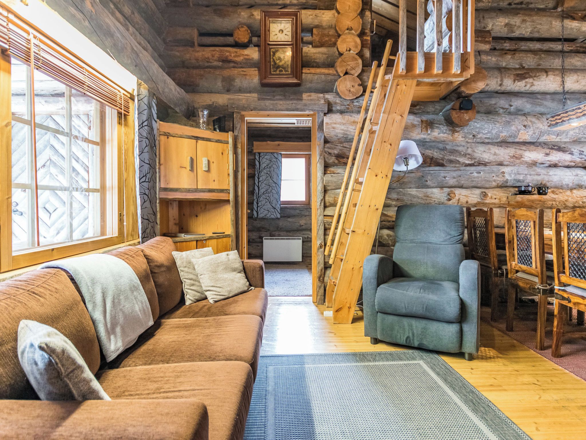 Ein Holzblockhaus-Interieur mit einer Couch, einem Sessel und einer Leiter, die zu einem Schlafboden führt.