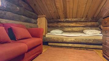 A log cabin interior with a red sofa, a bed with pillows, and a wooden dresser.