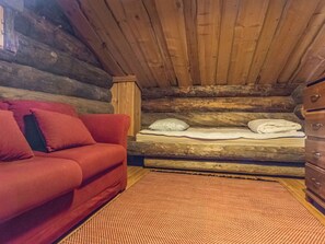 Ein Blockhaus-Interieur mit einem roten Sofa, einem Bett mit Kissen und einer Holzkommode.