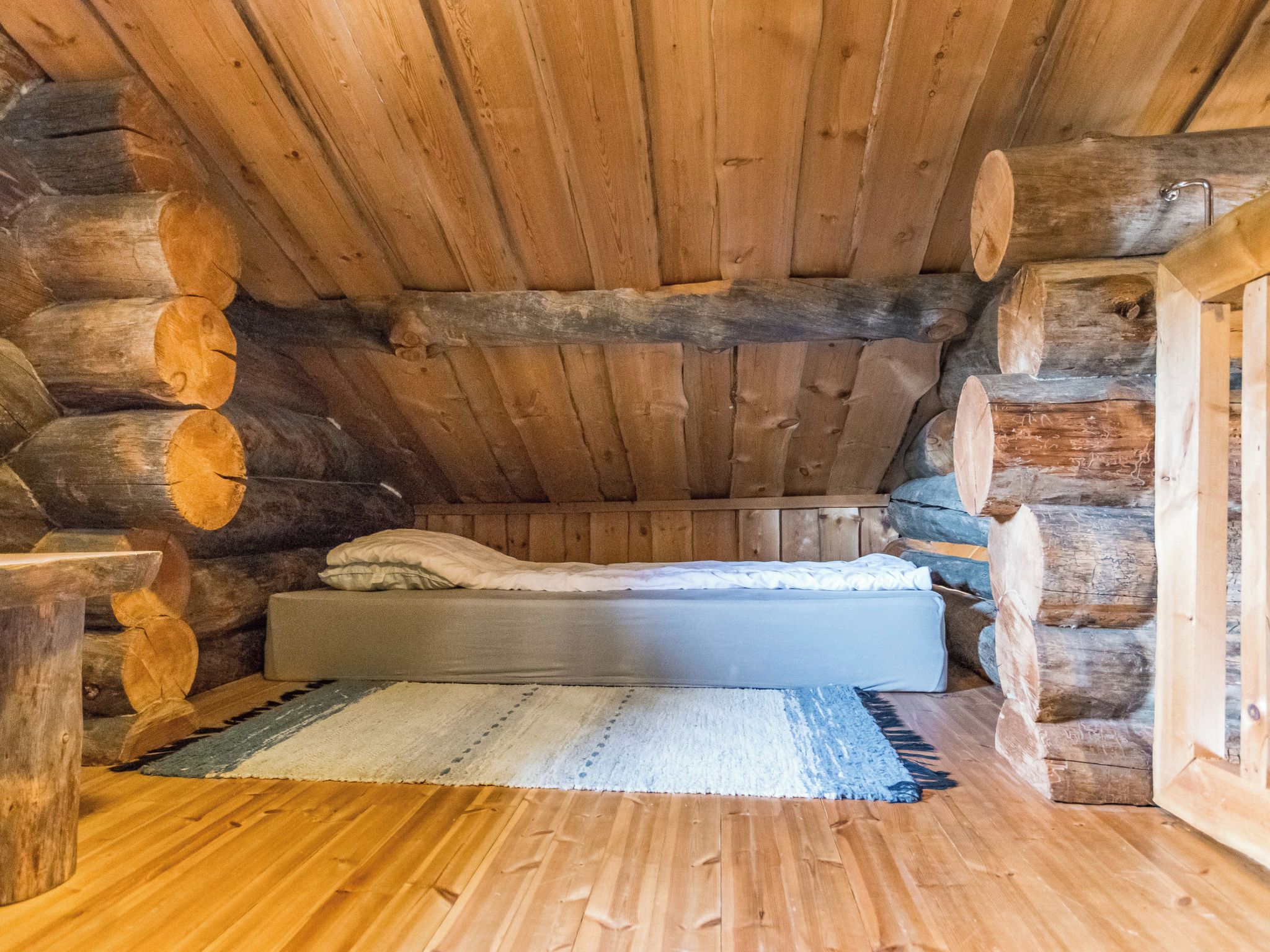 Ein Schlafzimmer in einer Blockhütte mit einem Bett, einem Teppich und Holzbalken als Wände.