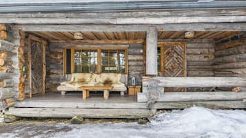 A log cabin with a wooden bench and a sofa outside, surrounded by snow.