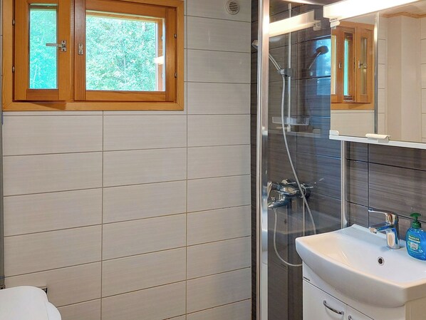Ein Badezimmer mit einer Duschkabine, einem Waschbecken mit Spiegel und einem Fenster über dem Waschbecken.