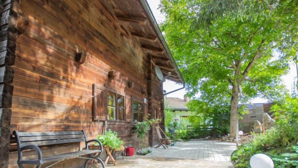 A rustic wooden building with a stone-paved entrance, a bench, and potted plants.