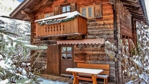 A wooden cabin with a balcony, a bench, and a door.