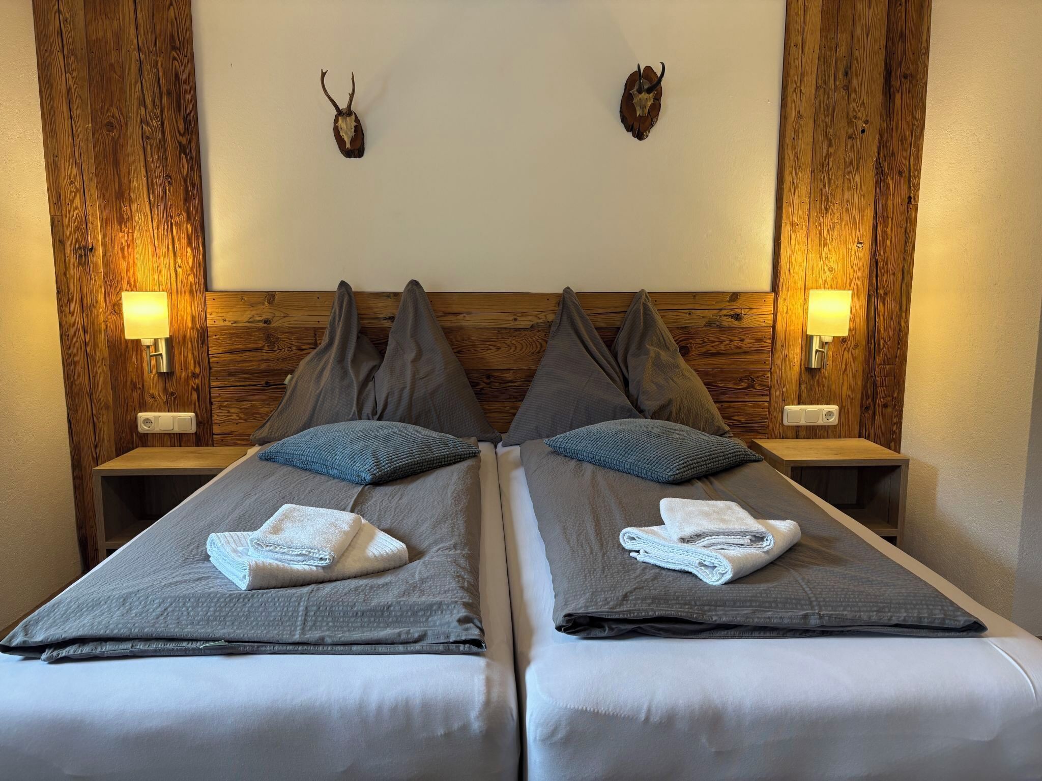 Une chambre double avec deux lits, des têtes de lit en bois et des lampes fixées au mur.