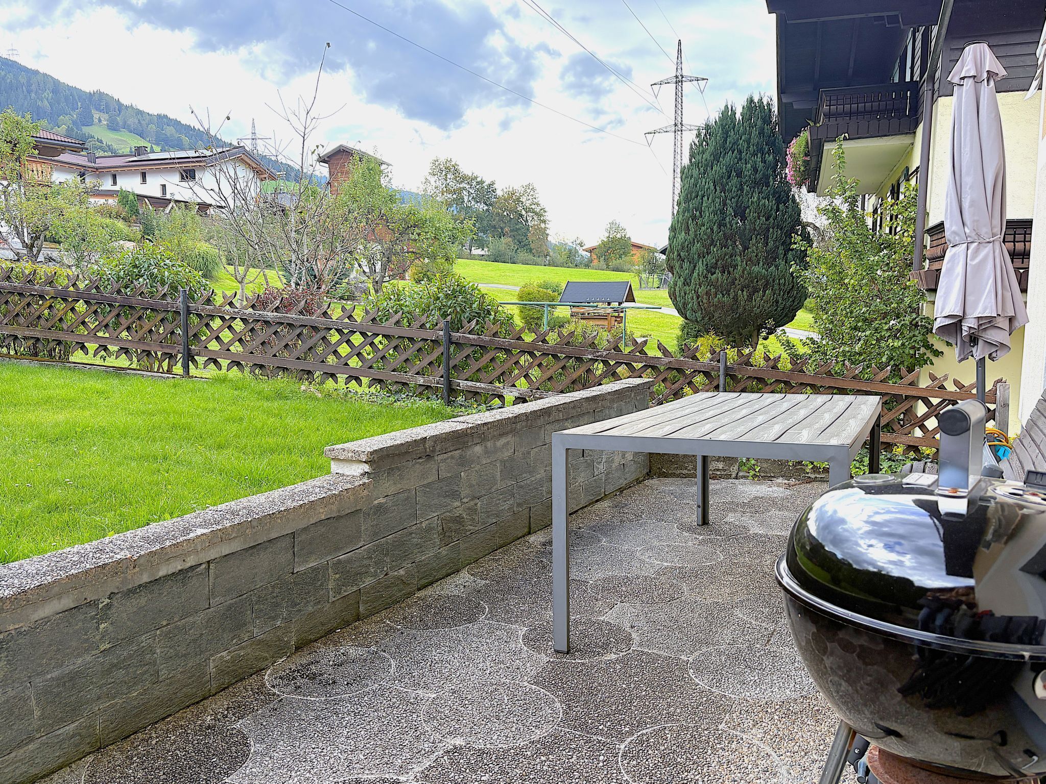 A patio area with a barbecue grill, a table, and a view of a green landscape with houses and trees.