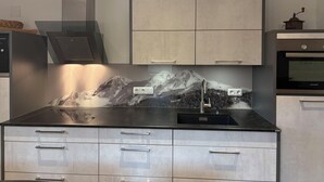 Ett modernt kök med ett stänkskydd som har ett bergsmotiv, rostfria vitvaror och en inbyggd ugn.