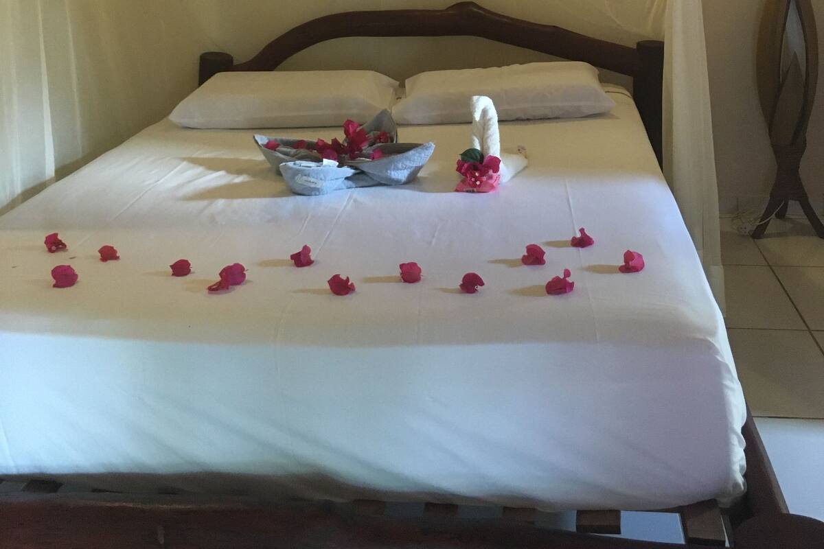 A bed with white linens, a canopy, and a bowl of fruit and flowers.