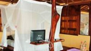 Una habitación con techo de madera, una cama con dosel blanco, una pequeña mesa con un ordenador y un banco de madera.