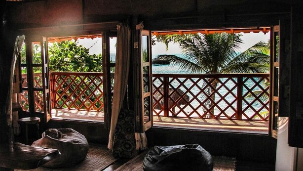 Una habitación con piso de madera, una cama y un ventanal con vista a una palmera y una piscina.
